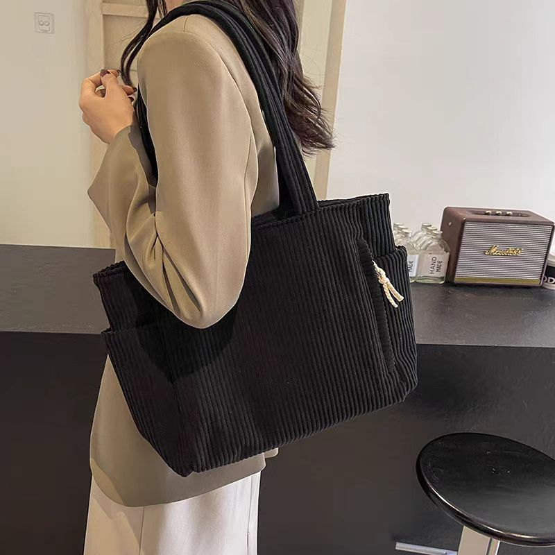 Women carrying a black corduroy tote bag with pockets on her shoulder
