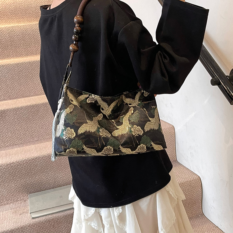 Woman carrying a black Pillow-style shoulder bag with flying crane pattern with a beaded handle and tassel on her shoulder