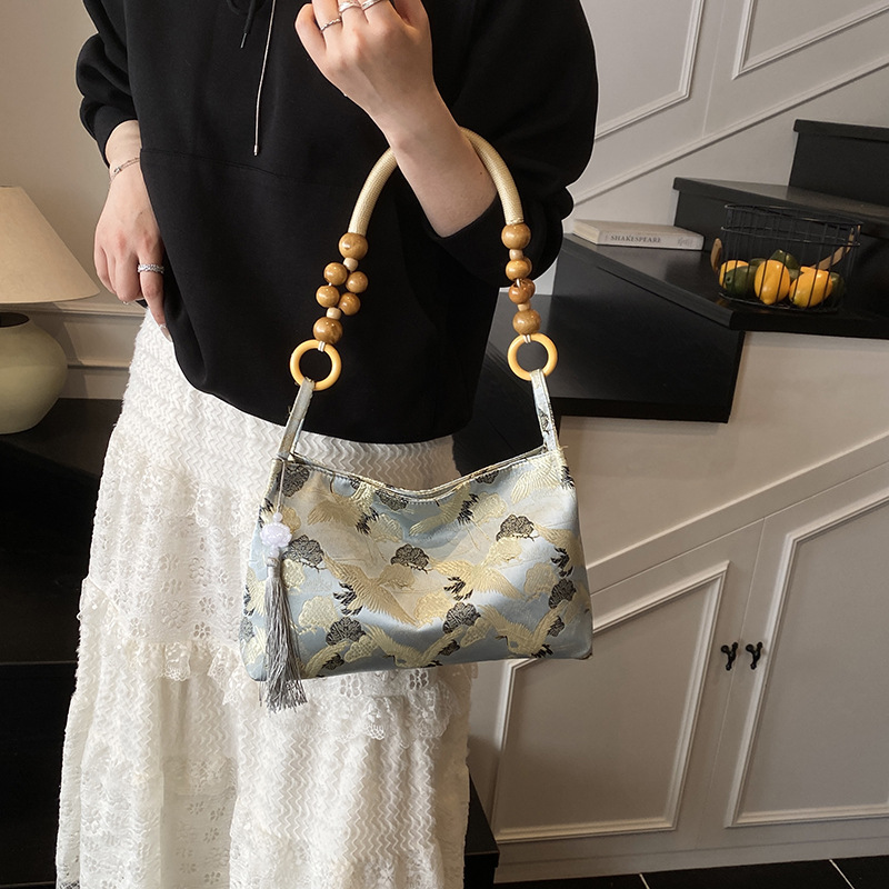 Woman carrying a blue Pillow-style shoulder bag with flying crane pattern with a beaded handle and tassel on her arm