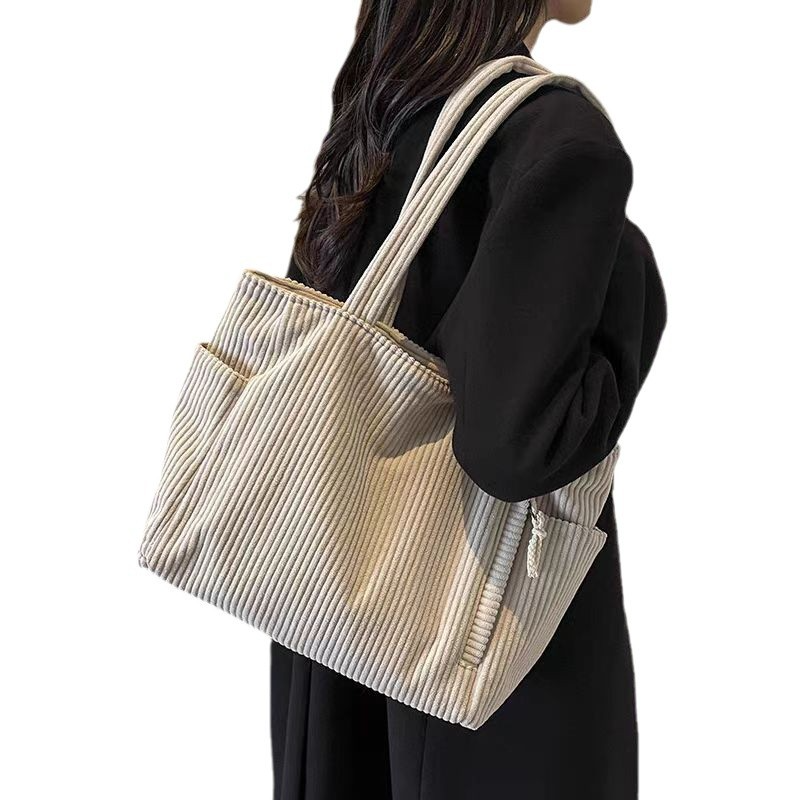 Woman carrying a beige corduroy tote bag with pockets on her shoulder