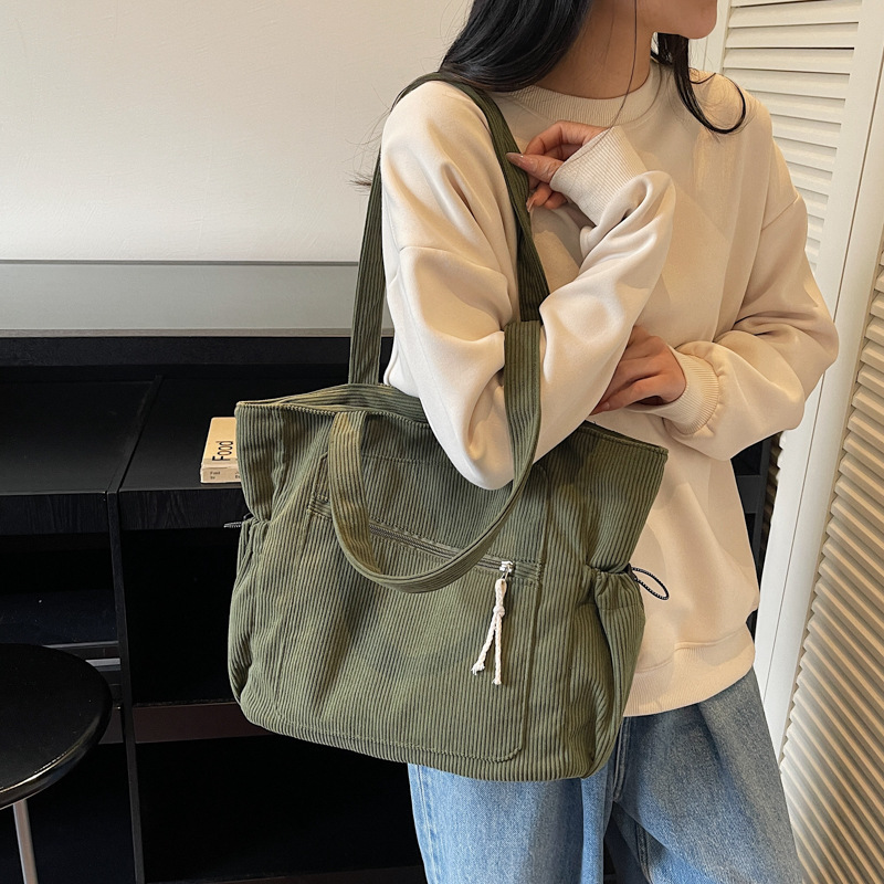 Women carrying a green corduroy tote bag with zipper and side slouchy pockets on her shoulder